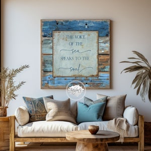 Peut inclure: Un canapé blanc avec des coussins et une table basse en bois devant. Un panneau en bois bleu et brun avec le texte "The voice of the sea speaks to the soul" est accroché au mur derrière le canapé.