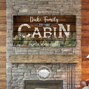 May include: A rustic wooden sign with the text "Duke Family Cabin Est. 1986 Hawley, Pennsylvania" in white lettering. The sign has a watercolor background of trees and a wooden plank texture.