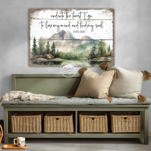 May include: A wood sign with a watercolor painting of a forest scene with mountains, trees, and a lake. The sign has the text "and into the forest I go. To lose my mind and find my soul" and "JOHN MUIR".