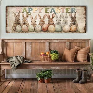 May include: A rustic wooden sign with the words "HAPPY EASTER" above a row of seven bunnies holding Easter eggs. The bunnies are various shades of brown and gray. The sign is displayed above a wooden bench with pillows and a basket of fruit.