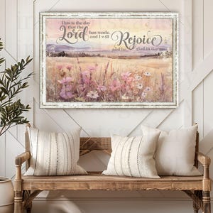 Peut inclure: Une impression d'art encadrée avec un cadre blanc vieilli. L'œuvre représente un champ de fleurs sauvages roses et jaunes, avec le texte "This is the day that the Lord has made, and I will rejoice and be glad in it."