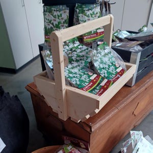 May include: A wooden carrying basket with a handle, filled with packets of flower bulbs. The packets are labelled with the names "10 Nicolaas Mathie" and "5 Ozark Angels".