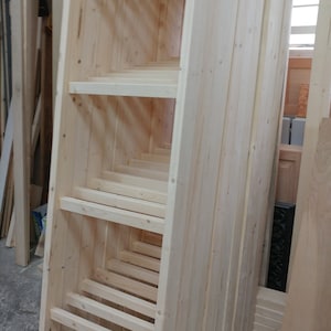 May include: A stack of unfinished wooden planks, likely for building a shelf or other woodworking project. The planks are arranged in a vertical stack, with the ends of the planks visible. The planks are all the same width and thickness, and they are all made of the same type of wood.