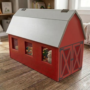 May include: A red wooden toy barn with a gray roof and three small windows. The barn doors are decorated with gray cross-shaped accents. The windows have wire mesh and show glimpses of toys inside. A charming farm-themed toy.