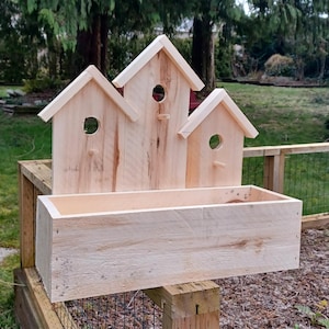 Op de afbeelding: Een houten vogelhuisje-plantenbak met drie vogelhuisjes bovenop en een rechthoekige plantenbak eronder. De vogelhuisjes zijn gemaakt van natuurlijk hout en hebben kleine openingen waar vogels naar binnen kunnen. De plantenbak is ook gemaakt van natuurlijk hout en heeft een lichtbruine afwerking.