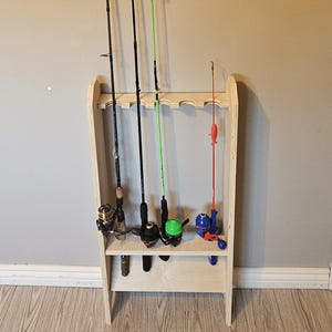 Op de afbeelding: Een houten hengelrek met meerdere hengels. Het rek is gemaakt van lichtgekleurd hout en heeft sleuven om de hengels vast te houden. Er worden verschillende hengels van verschillende kleuren en maten getoond.