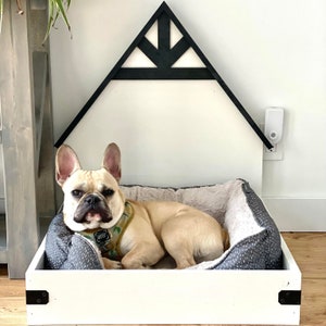May include: A white dog bed with a black and white geometric design on the top. The bed is in a white wooden frame with a black geometric design on the top. A French bulldog is laying in the bed.