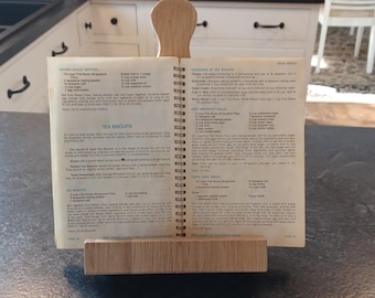 Könnte beinhalten: Ein hölzerner Kochbuchständer hält ein offenes Kochbuch auf einer Küchenarbeitsplatte. Das Kochbuch ist zu einem Rezept für "Tea Biscuits" aufgeschlagen. Der Ständer ist aus hellem Holz gefertigt und hat ein schlichtes, funktionales Design.