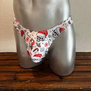 May include: White thong underwear with a Christmas-themed print featuring skulls wearing Santa hats, candy canes, snowflakes, and hearts.