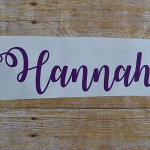 May include: Purple vinyl decal with the name "Hannah" written in a cursive font.