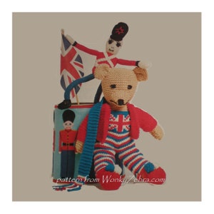 May include: A crocheted teddy bear wearing a red and blue striped outfit with a Union Jack design. The bear is holding a blue scarf and sitting next to a toy soldier and a Union Jack flag.
