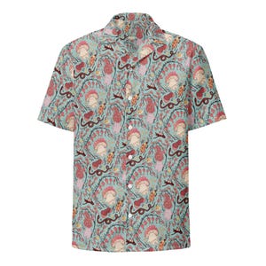 May include: Short-sleeved button-down shirt with a whimsical pattern of mushrooms, vines, and other botanical elements in shades of red, pink, and beige on a light blue background. The shirt has a classic collar and a button-up front.