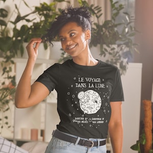 May include: Black t-shirt with a white graphic of a moon with a telescope in its eye. The text "LE VOYAGE DANS LA LUNE" is above the moon. The text "DIRECTED BY GEORGES MÉLIES SOUNDTRACK BY TYAN LOMBARD" is below the moon.