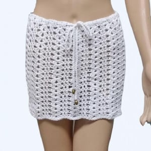 May include: A white, open-weave crochet skirt with a drawstring waist. The skirt is made of a light-colored yarn and features a scalloped hemline. The drawstring has gold-colored beads. This skirt is suitable for beachwear or summer apparel.