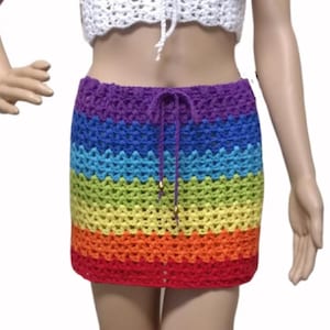May include: A rainbow-colored crochet skirt with a drawstring waist. The skirt features horizontal stripes in red, orange, yellow, green, blue, and purple. The skirt is a mini-skirt style.