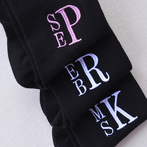 May include: Three pairs of black socks with embroidered initials. The top pair has the initials "SE" in pink, the middle pair has the initials "EB" in white, and the bottom pair has the initials "MS" in white.