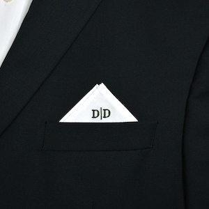 May include: A white pocket square with the embroidered initials "D|D" is neatly folded in a black suit pocket. The suit is paired with a white dress shirt, creating a classic and elegant look.
