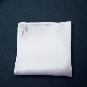 May include: A white pocket square with the initials "N.B." embroidered in the upper left corner.