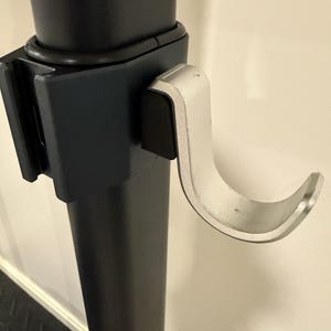 May include: Close-up of a black metal support post with a silver-colored hook attached. The hook is curved and appears to be made of metal. The post has a rectangular bracket and a black rubber bumper.