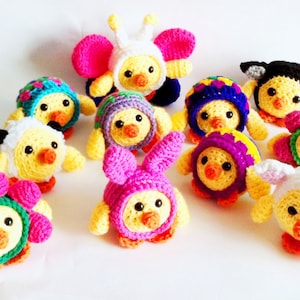 May include: A collection of 10 crocheted chicks wearing different colorful hats, including a bee, a flower, a bunny, and a black and white cow.