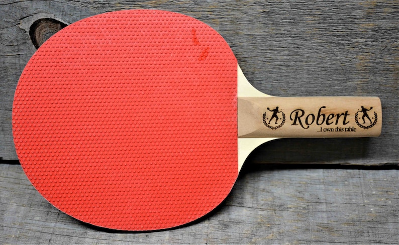 May include: A red and wooden ping pong paddle with the name "Robert" and the text "I own this table" engraved on the handle.