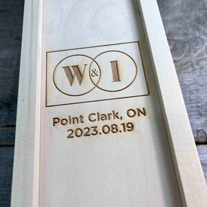 May include: A wooden box with a personalised inscription. The inscription reads "W&I" in a circle with a date of "2023.08.19" and the location "Point Clark, ON".