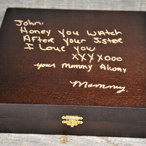 Pode incluir: Uma caixa de madeira castanho escura com uma trava dourada. A parte superior da caixa tem uma mensagem escrita &agrave; m&atilde;o em tinta dourada que diz "John, Honey you watch After your sister I love you xxx x000 your mommy Alway Mommy."