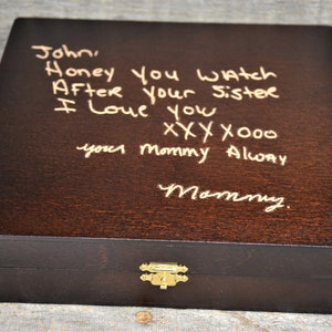 May include: A dark brown wooden box with a gold latch. The top of the box has a handwritten message in gold paint that reads "John, Honey you watch After your sister I love you xxx x000 your mommy Alway Mommy."