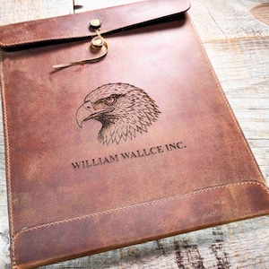 Peut inclure: Un porte-documents en cuir marron avec une fermeture à rabat et un fermoir en laiton. Le devant présente une tête d'aigle gravée et le texte "WILLIAM WALLCE INC."