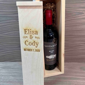 May include: A wooden wine box with a hinged lid, engraved with the names "Elisa & Cody" and the date "October 7, 2023". The box contains a bottle of Santa Julia Reserva Malbec wine.