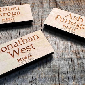 May include: Three wooden name tags with the names "Robel Arega", "Ash Panegal", and "Jonathan West" engraved on them. Each tag has the logo "PLUS POWER" printed below the name.