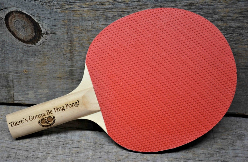 May include: A wooden ping pong paddle with a red rubber surface and the text "There's Gonna Be Ping Pong?" engraved on the handle.