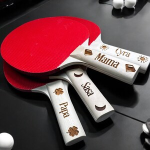 May include: Three red and white ping pong paddles with personalized names: "Papa", "Sasa", and "Mama Cyra".