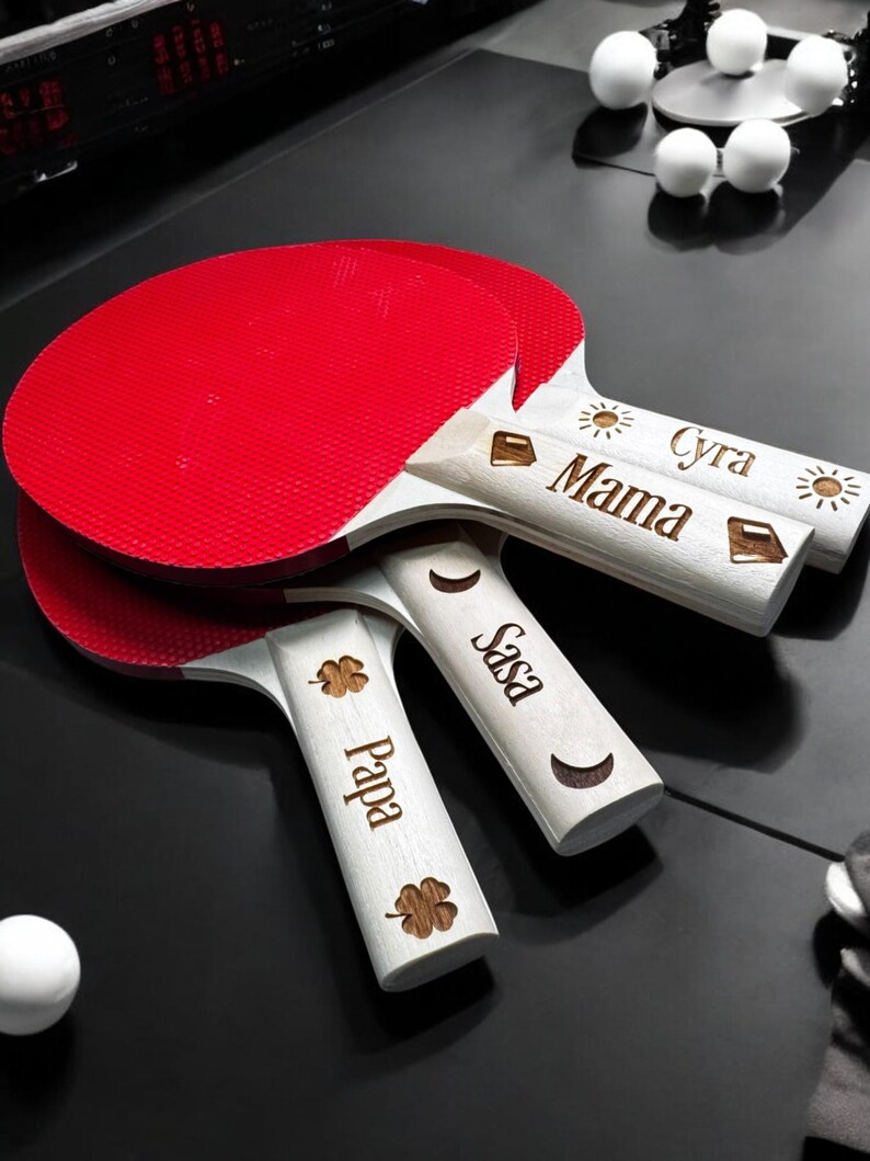 May include: Three red and white ping pong paddles with personalized names: "Papa", "Sasa", and "Mama Cyra".