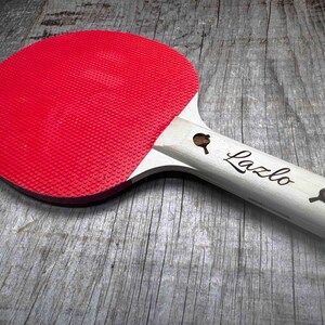 May include: A red and white table tennis paddle with the name "Lazlo" engraved on the handle.