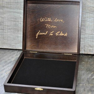 Pode incluir: Uma caixa de madeira castanho escuro com um interior de veludo preto. A tampa est&aacute; aberta e tem uma inscri&ccedil;&atilde;o dourada que diz "With love, Mom Jewel La Clark".