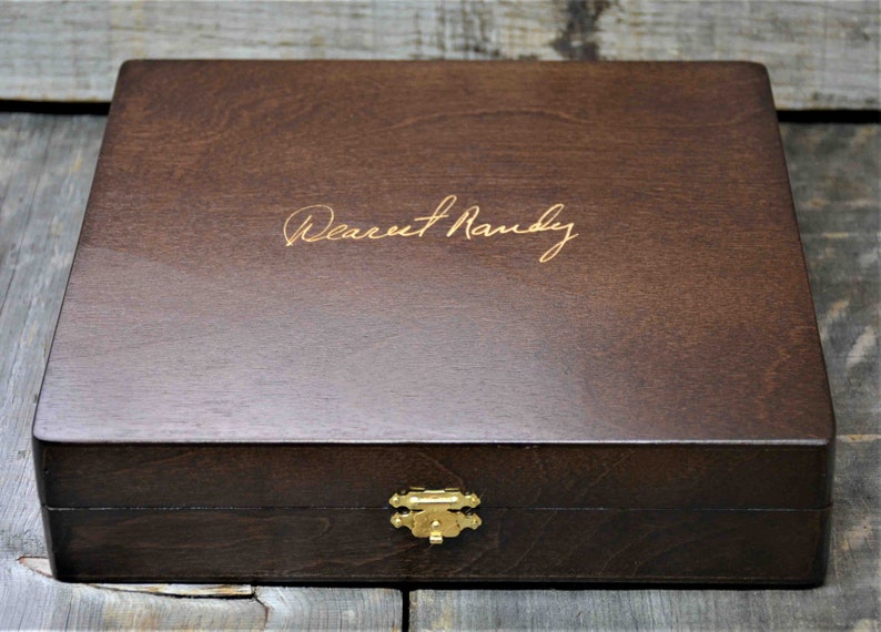 Pode incluir: Uma caixa de madeira marrom escura com uma trava dourada e a inscri&ccedil;&atilde;o "Dearest Randy" na parte superior.
