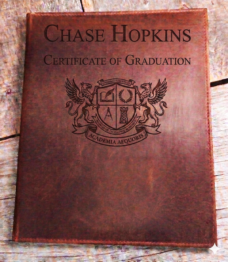May include: A brown leather certificate holder with the name "Chase Hopkins" and "Certificate of Graduation" embossed on the cover. The holder features a detailed crest with two winged creatures and the text "Academia Aequoris".