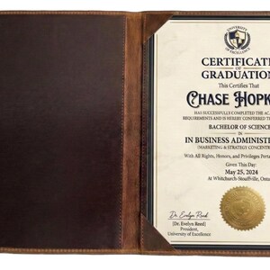 May include: A brown leather certificate holder, open to reveal a diploma. The certificate is for Chase Hopkins, Bachelor of Science in Business Administration, dated 25 May, 2024. The holder has a darker interior.