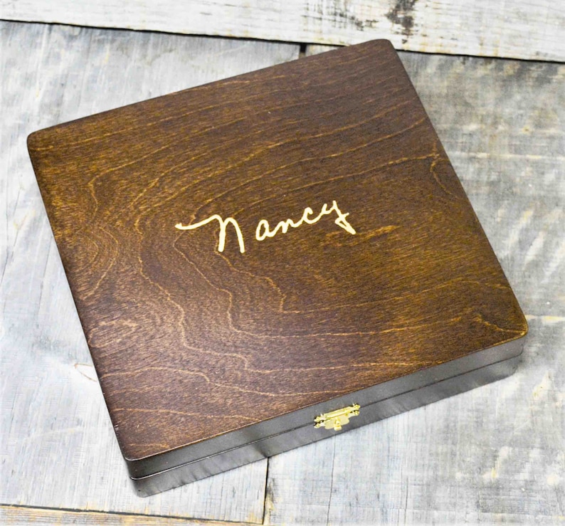 Pode incluir: Uma caixa de madeira castanho escuro com uma trava dourada. A caixa tem o nome "Nancy" gravado na parte superior em letras douradas.