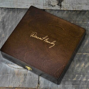 Pode incluir: Uma caixa de madeira castanho escuro com uma trava dourada. A caixa tem uma inscri&ccedil;&atilde;o personalizada que diz "Dearest Randy".