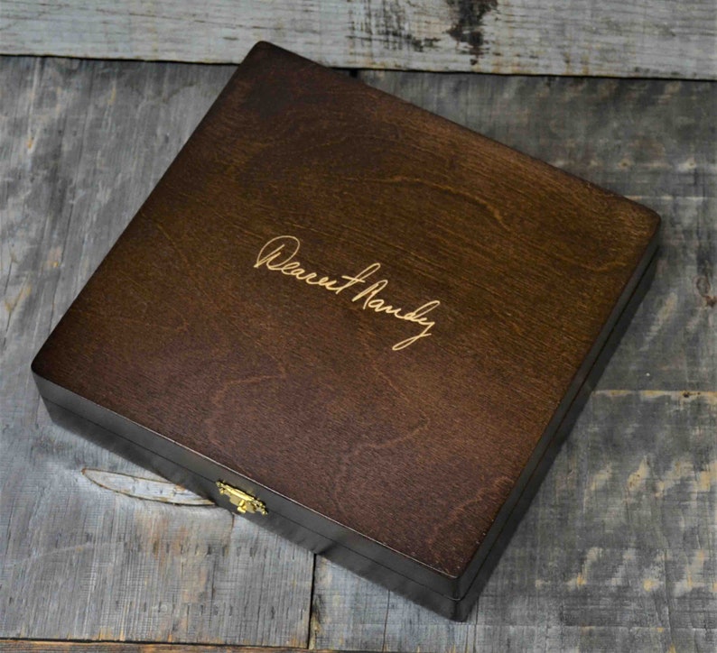 Pode incluir: Uma caixa de madeira castanho escuro com uma trava dourada. A caixa tem uma inscri&ccedil;&atilde;o personalizada que diz "Dearest Randy".