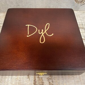 May include: A dark brown wooden box with a gold inscription that reads "Dyl".