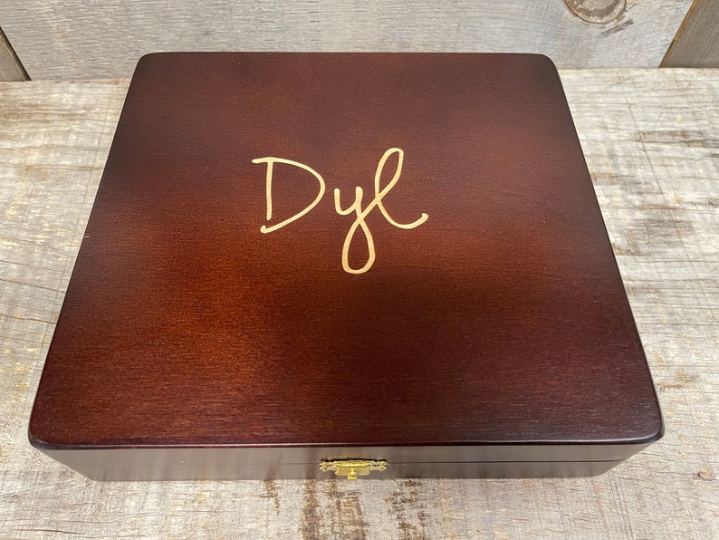 May include: A dark brown wooden box with a gold inscription that reads "Dyl".