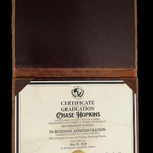 May include: A graduation certificate for Chase Hopkins, Bachelor of Science in Business Administration, presented in a brown leatherette folder. The certificate is dated May 25, 2024, and is from the University of Excellence.