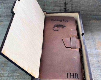May include: A brown leather-bound journal with the words "Fishing Log" and a fly fishing lure engraved on the front cover. The journal is in a wooden box with the initials "THR" engraved on the front.