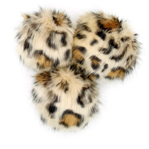 May include: Three fluffy pom poms with a leopard print pattern. The pom poms are beige, brown, and black.