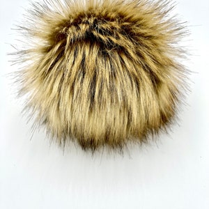 May include: A fluffy brown faux fur pom pom. The pom pom is made of soft, synthetic fur and is perfect for adding a touch of warmth and style to any hat or accessory.
