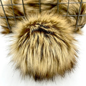 May include: A large, fluffy faux fur pom pom in a light brown and dark brown colour. The pom pom is made of soft, plush fur and is perfect for adding a touch of luxury to any project.