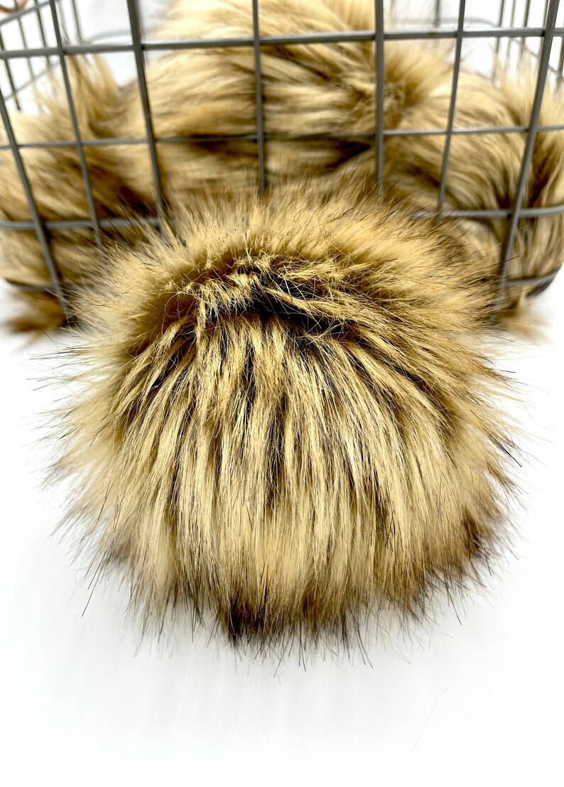 May include: A large, fluffy faux fur pom pom in a light brown and dark brown colour. The pom pom is made of soft, plush fur and is perfect for adding a touch of luxury to any project.